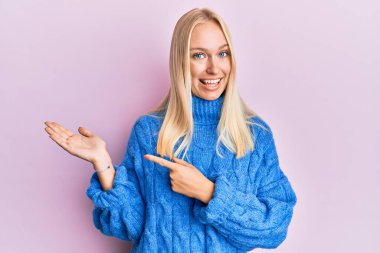 Kışın yün kazak giyen genç sarışın kız kameraya hayret ediyor ve gülümsüyor.. 