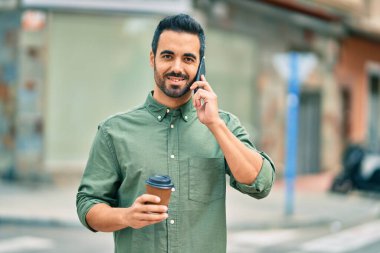 Genç İspanyol adam akıllı telefondan konuşuyor. Şehirde kahve içiyor..