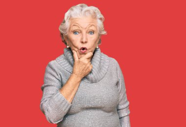 Kış süveteri giyen yaşlı, gri saçlı kadın elleri çenesinde olan inançsızlıktan, şaşkınlıktan ve şaşkınlıktan büyülenmiş görünüyor. 