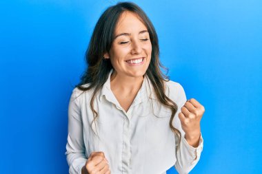 Genç esmer kadın gündelik giysiler giyiyor. Başarının şaşkınlığını ve şaşkınlığını kutluyor. Kolları havada ve gözleri kapalı. 