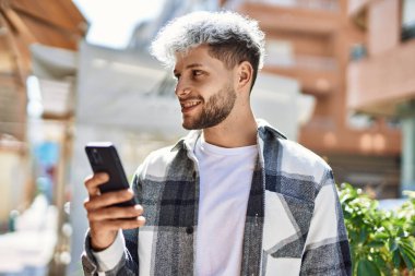 Genç İspanyol adam şehirde akıllı telefon kullanarak mutlu gülümsüyor..