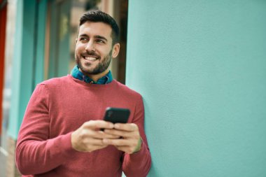 Genç İspanyol adam şehirde akıllı telefon kullanarak mutlu gülümsüyor..