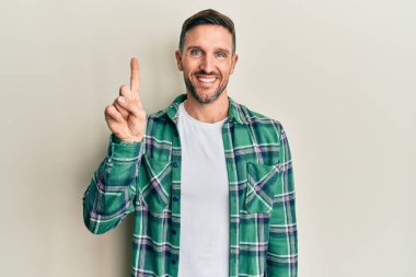 Sakallı, sıradan kıyafetler giyen yakışıklı bir numaralı parmağı gösterip işaret eden, kendinden emin ve mutlu gülümseyen adam.. 