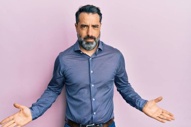 Orta yaşlı, sakallı, gri saçlı, iş kıyafetlerinden bihaber ve elleri havada, kafası karışmış bir adam. şüphe kavramı. 