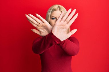 Gündelik kıyafetler giyen genç sarışın kadın. Reddedilmiş yüz ifadesi. Kollarını kavuşturup, avuçlarını çaprazlayarak negatif işaret veriyor. 