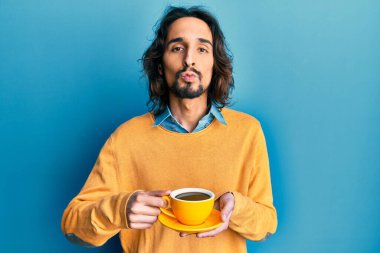 Latin asıllı genç bir adam bir fincan kahve içip kameraya bakarak öpüşürken sevimli ve seksi oluyor. aşk ifadesi. 