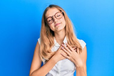 Gündelik kıyafetler ve gözlük takan, göğsünde elleri göğsünde gülümseyen, yüzünde minnet ifadesi olan güzel beyaz bir kız. sağlık kavramı. 