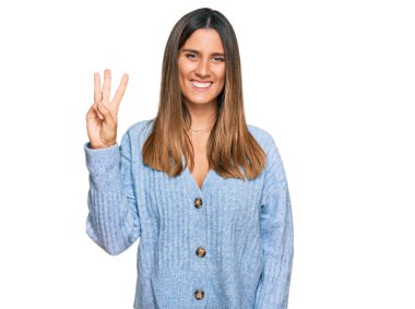 Gündelik kıyafetler giyen genç bir kadın üç numarayı gösterip işaret ederken kendinden emin ve mutlu bir şekilde gülümsüyor.. 