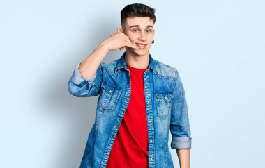 Kulakları genişlemiş, sıradan bir kot ceket giymiş, telefonla el ve parmaklarıyla gülümseyen, telefonda konuşan beyaz bir çocuk. iletişim kavramları. 