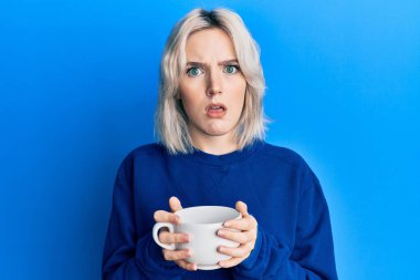 Bir fincan kahve içen genç sarışın kız habersiz ve kafası karışık bir ifade takınıyor. şüphe kavramı. 