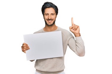 Boş afiş tutan genç İspanyol bir adam bir fikre ya da mutlu yüzle işaret eden bir soruya şaşırdı. 