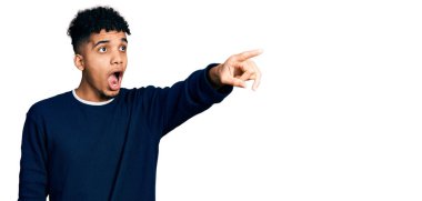 Genç, Afro-Amerikalı, günlük giysiler giymiş, parmaklarını göstererek şaşırmış, ağzı açık, şaşırmış, ön tarafta bir şey var. 