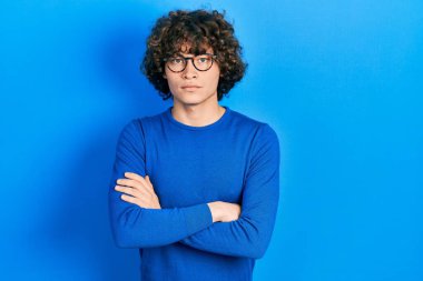 Gündelik kıyafetler giyen, gözlüklü, kuşkucu ve gergin, yüzünde çapraz kollarla onaylanmayan bir ifade olan yakışıklı bir genç. negatif kişi. 