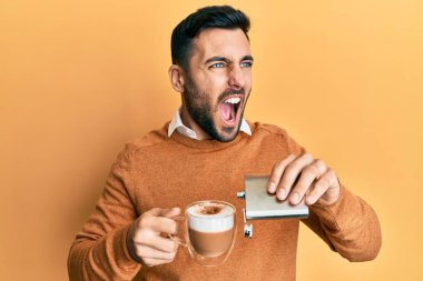 Genç İspanyol bir adam alkollü bir fincan kahve içiyor kızgın ve öfkeli çığlıklar atıyor sinirden köpürüyor ve öfkeyle bağırıyor. öfke ve agresif konsept. 