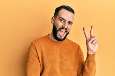 Sakallı, sıradan bir kazak giyen, gülümseyen ve kameraya bakıp zafer işareti yapan genç bir adam. İki numara.. 