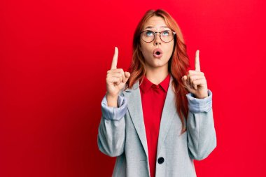 İş ceketi ve gözlük takan genç kızıl saçlı kadın hayret ve şaşkınlık içinde başını kaldırıp parmaklarıyla işaret etti ve kollarını kaldırdı.. 