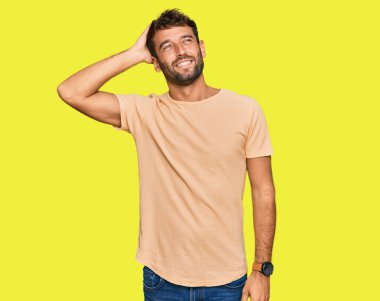 Sakallı, rahat tişörtlü, yakışıklı, kendine güvenen, el hareketleriyle saçlara dokunan çekici ve şık görünümlü bir genç. 