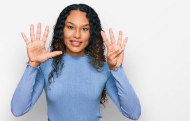 Kıvırcık saçlı, günlük kıyafetler giyen, dokuz numaralı parmaklarıyla işaret eden, kendinden emin ve mutlu gülümseyen genç İspanyol kadın.. 