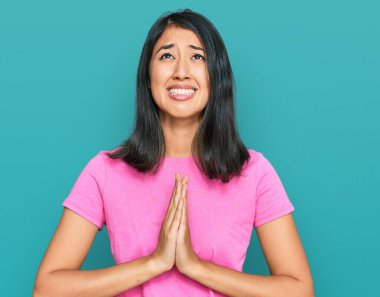 Güzel Asyalı genç bir kadın, günlük pembe tişörtler giyip elleri bağlı yalvarıyor ve dua ediyor. Yüzünde umut ifadesi var. Çok duygusal ve endişeli. Yalvarıyor. 