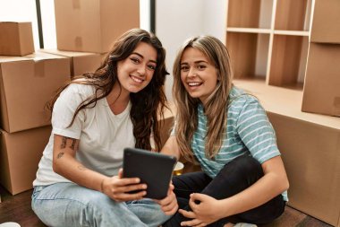 Genç çift yeni evinde dokunmatik ped kullanarak mutlu gülümsüyor..