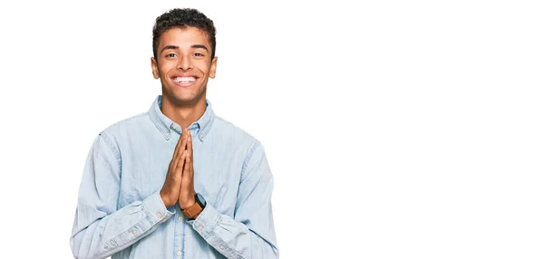 若いですハンサムなアフリカ系アメリカ人男性を身に着けていますカジュアルな服を着て手で祈る一緒に許し笑顔自信を求めて — ストック写真