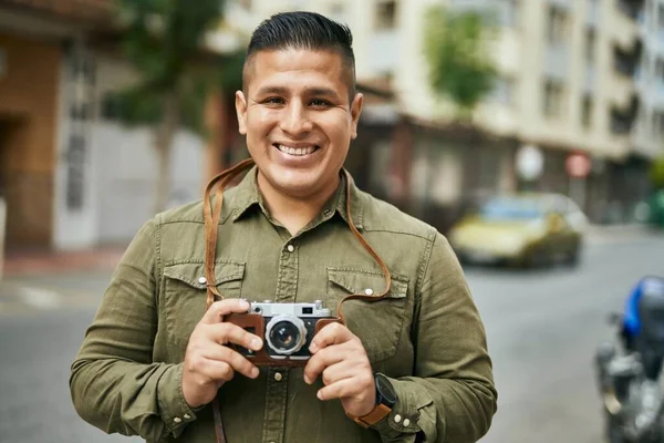 Young latin tourist man smiling happy using vintage camera at the city.