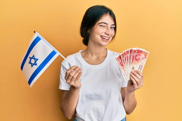 Junge Kaukasische Frau Mit Israel Flagge Und Schekel Banknoten Zwinkernd — Stockfoto