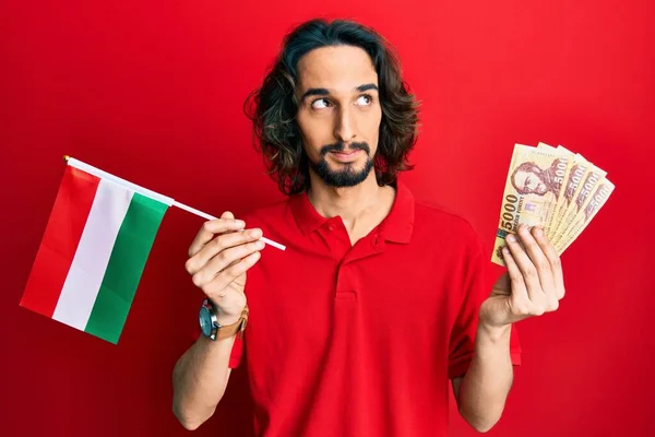 Joven Hombre Hispano Sosteniendo Una Bandera Hambrienta Forintos Sonriendo Mirando —  Fotos de Stock