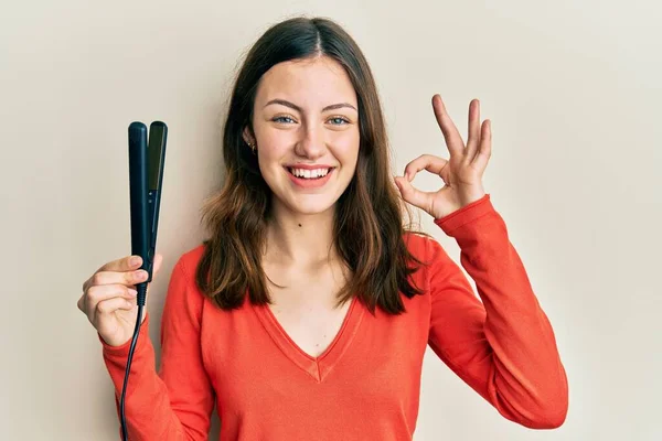 Młoda Brunetka Kobieta Trzyma Prostownica Włosów Robi Znak Palcami Uśmiechnięty — Zdjęcie stockowe