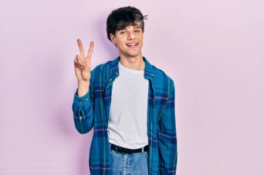 Yakışıklı hippi genç adam, günlük beyaz tişört ve klasik tişört giyiyor. İki numarayı gösterip, parmaklarını gösterirken kendine güvenen ve mutlu gülümseyen.. 