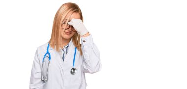 Güzel beyaz kadın doktor üniforması giyiyor ve steteskop yorgun burnu ve gözleri ovuşturuyor yorgunluk ve baş ağrısı hissediyor. Stres ve hüsran kavramı. 