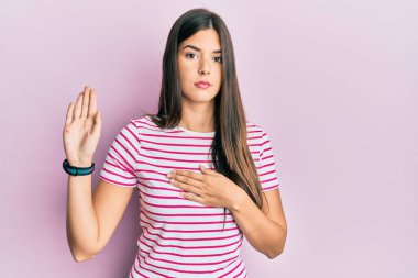 Genç esmer kadın pembe arka plan üzerine gündelik kıyafetler giyip el pençe divan yemin ederek sadakat yemini ediyor. 