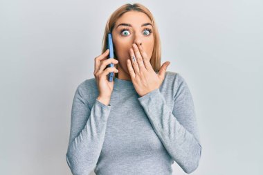 Kafkasyalı genç bir kadın akıllı telefonla konuşuyor ağzını eliyle kapatıyor, şok geçiriyor ve hata yapmaktan korkuyor. şaşırmış ifade 