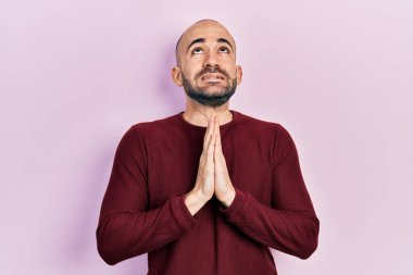 Genç kel adam gündelik giysiler giyip elleri bağlı yalvarıyor ve dua ediyor. Yüzünde umut ifadesi var. Duygusal ve endişeli. Yalvarıyor. 