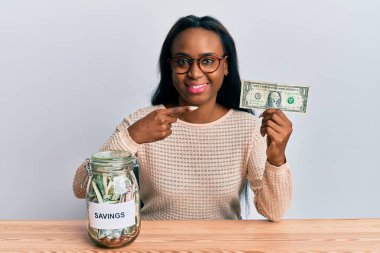 Elinde dolar ve kavanozla gülümseyen, mutlu, eli ve parmağı olan Afrikalı genç bir kadın. 