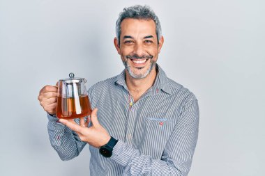 Gri saçlı yakışıklı bir adam elinde geleneksel çay demliği tutuyor. Pozitif ve mutlu görünüyor. Kendine güvenen bir gülümsemeyle dişlerini gösteriyor. 