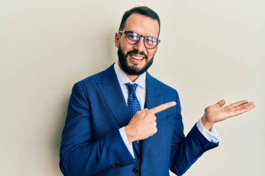 Sakallı, takım elbiseli ve kravatlı genç adam kameraya hayret ediyor ve gülümsüyor.. 