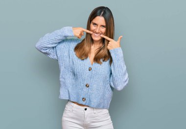 Gündelik kıyafetler giyen, neşeli gülümseyen, parmaklarıyla ve ağzıyla işaret eden genç bir kadın. diş sağlığı kavramı. 