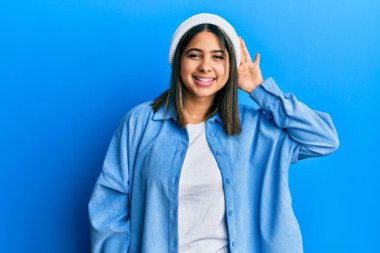 Şirin yün şapkalı, ağzı kulaklarında, dedikoduları ve dedikoduları dinleyen genç Latin bir kadın. Sağırlık kavramı. 