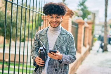 Genç Afrikalı Amerikalı iş adamı şehirde akıllı telefon kullanarak su tutuyor..