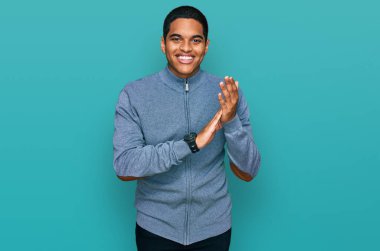 Genç, yakışıklı İspanyol adam, sıradan bir kazak giyiyor, alkışlıyor, alkışlıyor, mutlu, mutlu ve gururlu elleri biraraya getiriyor. 