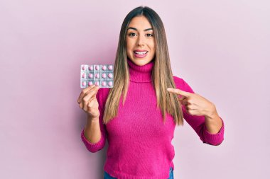 Genç İspanyol kadın elinde haplarla gülümsüyor. 