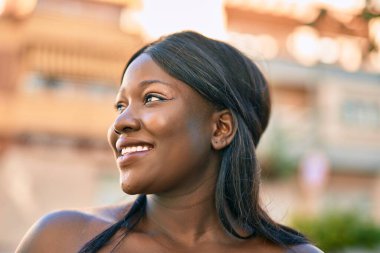 Genç Afrikalı Amerikalı kadın gülümseyerek şehirde mutlu mesut duruyor..