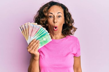 Orta yaşlı İspanyol kadın elinde Norveç kronu banknotları tutuyor. Korkmuş ve şaşkına dönmüş bir şekilde ağzı açık, inançsız bir yüz. 