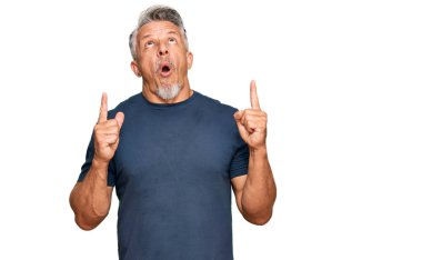 Orta yaşlı, gri saçlı, sıradan kıyafetler giyen, hayrete düşmüş, şaşırmış, parmaklarıyla işaret eden ve kollarını kaldıran bir adam.. 