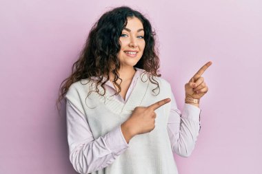 Kıvırcık saçlı genç esmer kadın. Günlük kıyafetler giyiyor. Gülümsüyor ve kameraya bakıyor.. 