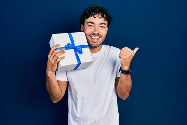 Jonge Spaanse Man Houdt Geschenk Wijzen Duim Naar Zijkant Glimlachen — Stockfoto