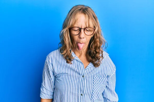中年金发女人穿着休闲装 戴着眼镜 带着滑稽的表情高兴地伸出舌头 情感概念 — 图库照片
