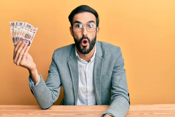 Jovem Hispânico Segurando Pesos Mexicanos Sentado Mesa Assustado Surpreso Com — Fotografia de Stock