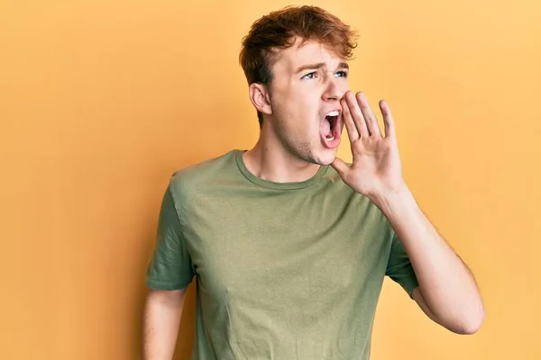 若い白人男性がカジュアルな緑のTシャツを着て大声で叫び 口の上に手で横に大声で叫ぶ コミュニケーションの概念 — ストック写真